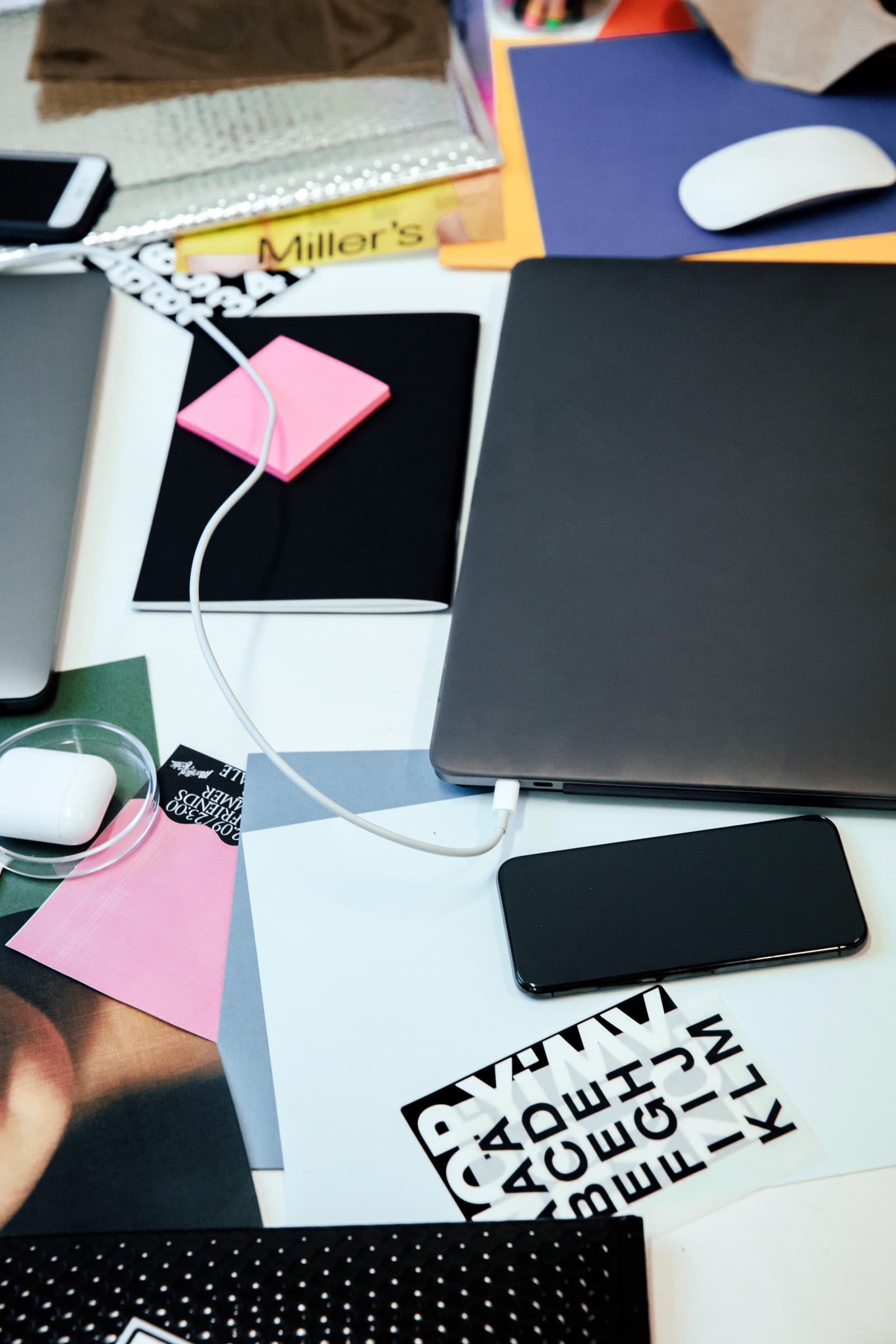 Bureau vu de haut : un ordinateur portable fermé relié à un câble de recharge, un téléphone, un carnet avec des post-it et des papiers