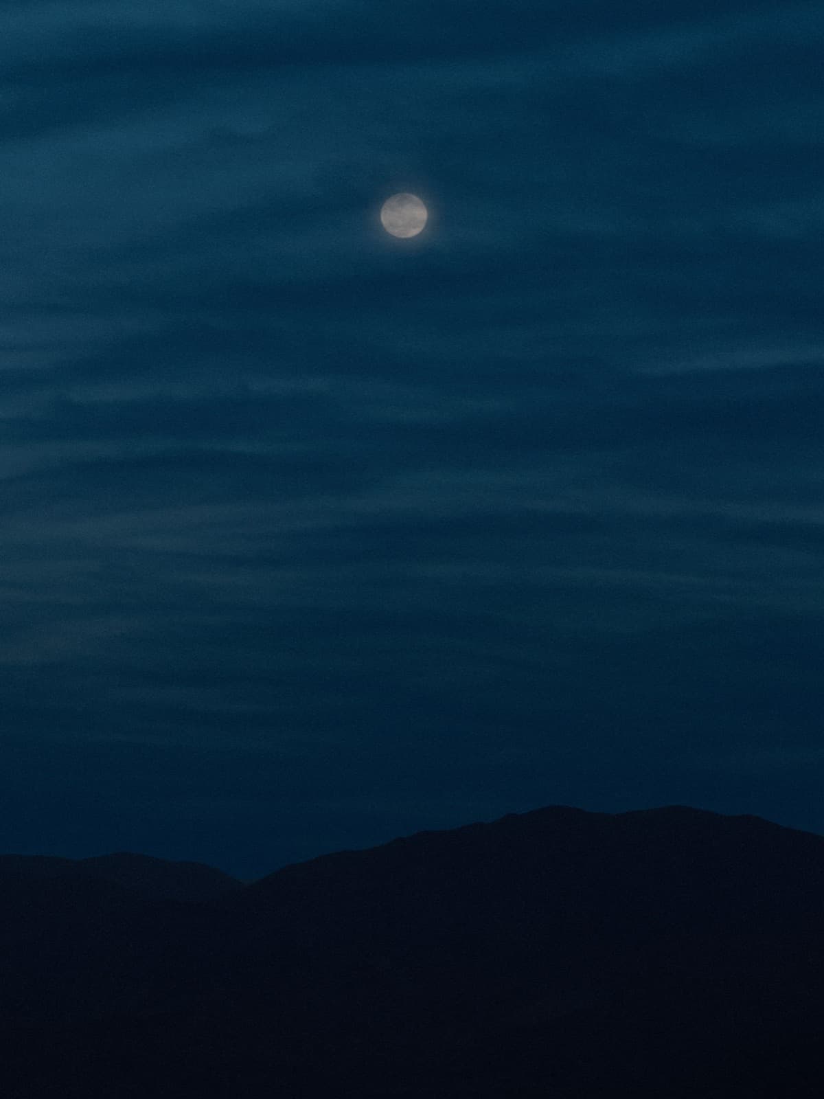 Pleine lune brillant à travers de fines traînées de nuages, bien au-dessus de la silhouette d'une crête montagneuse