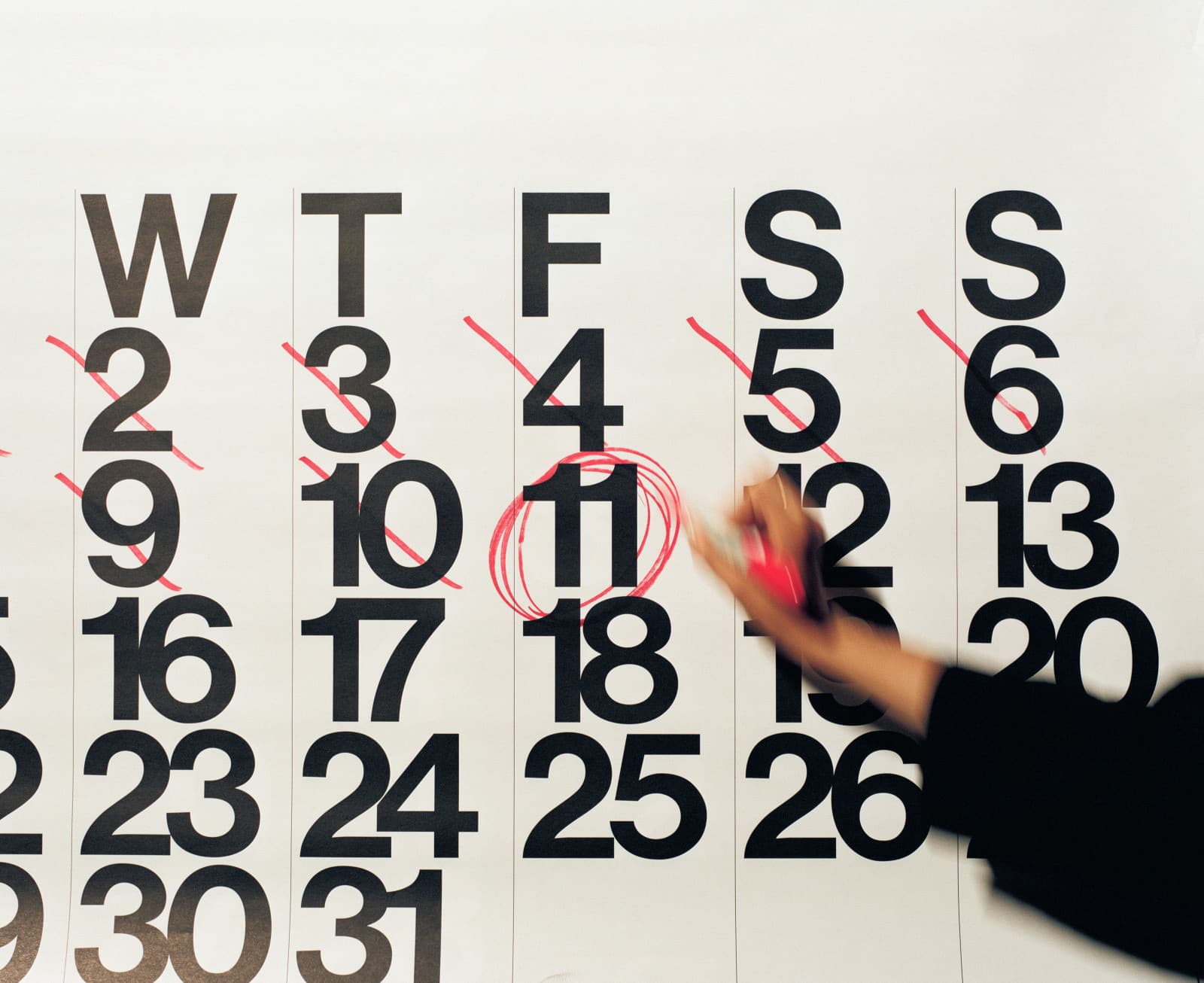 Main entourant le 11 au feutre rouge sur un grand calendrier mural, les jours précédents barrés
